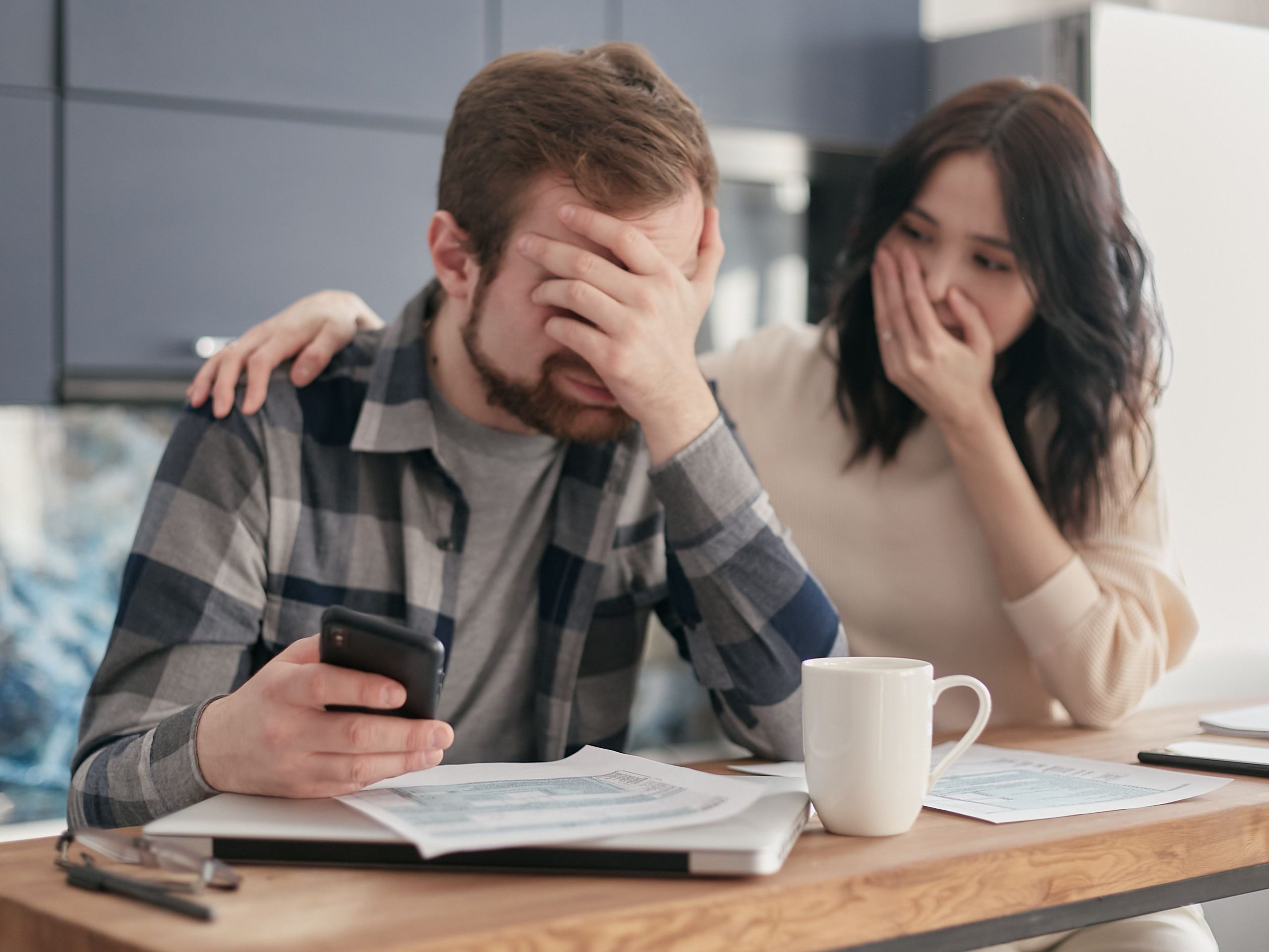 Un couple rapproche son relevé en ligne, le téléphone posé sur la table et son classeur de garanties
